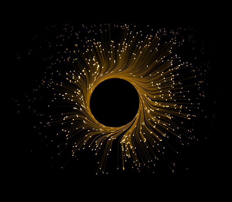 A circular burst of golden light trails radiates outward against a black background, reminiscent of the dynamic interplay in an Intelligent Converged Optical Network (ICON). Points of light scatter along the trails, adding a shimmering, galaxy-like effect.
