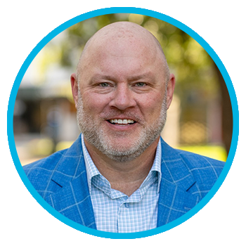 Meet Uniti Wholesale: A smiling bald man with a light beard wears a blue plaid suit jacket and light shirt, posed outdoors with a blurred background and a blue circular border around the image.