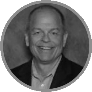 Black and white portrait photo of a middle-aged man smiling, wearing a suit jacket and collared shirt, inside a circular frame with a gray border. Meet Uniti Wholesale’s approachable professionalism in this striking image.