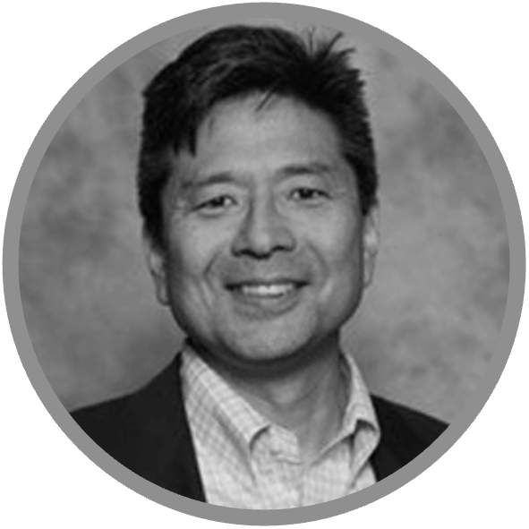 Black and white headshot of a man with short dark hair, wearing a suit jacket over a light-colored collared shirt, smiling at the camera. The image, in a circular frame with a plain background, introduces you to Meet Uniti Wholesale.