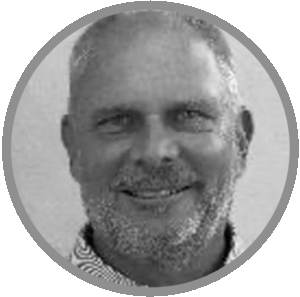 Black and white portrait of a middle-aged man with short hair and a beard, smiling at the camera. The image is circular with a gray border—Meet Uniti Wholesale’s approachable team.