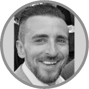 Black and white photo of a smiling man with short, dark hair and a beard, wearing a light-colored jacket. The image is circular with a gray border. Meet Uniti Wholesale in this classic portrait.