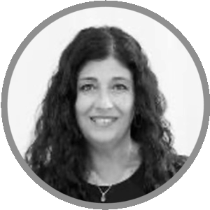 Meet Uniti Wholesale: Black and white portrait of a woman with long, curly dark hair, smiling, wearing a dark top and a necklace, inside a circular gray border.