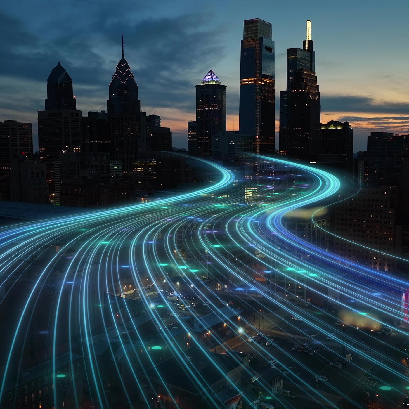 A city skyline at dusk with tall buildings, overlaid by blue and green glowing light trails that curve and flow above the streets, representing Uniti Wholesale’s nationwide network and seamless technology partnership.